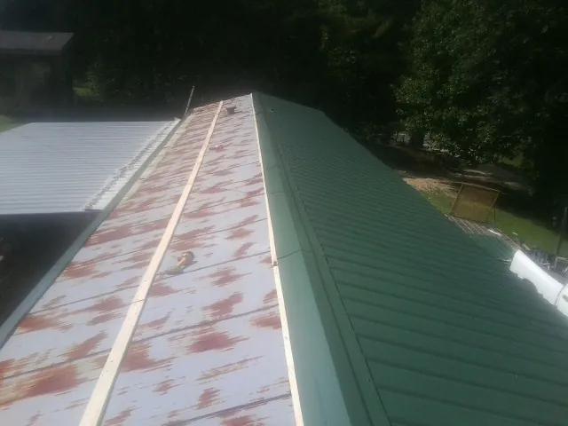 Old rusted panels beside newly installed green metal roofing — Wind Damage Roof Repair by Roofing Brothers in Malden