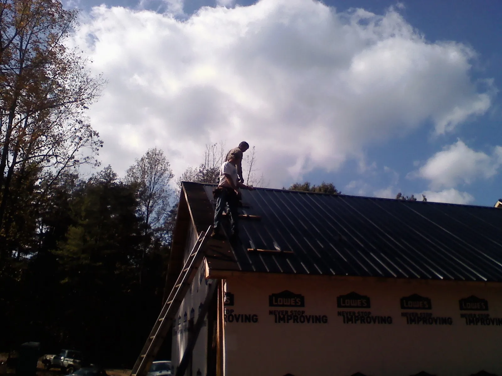 Roofer fastening dark metal panels high against a cloudy sky, from a Roof Inspection job in Malden