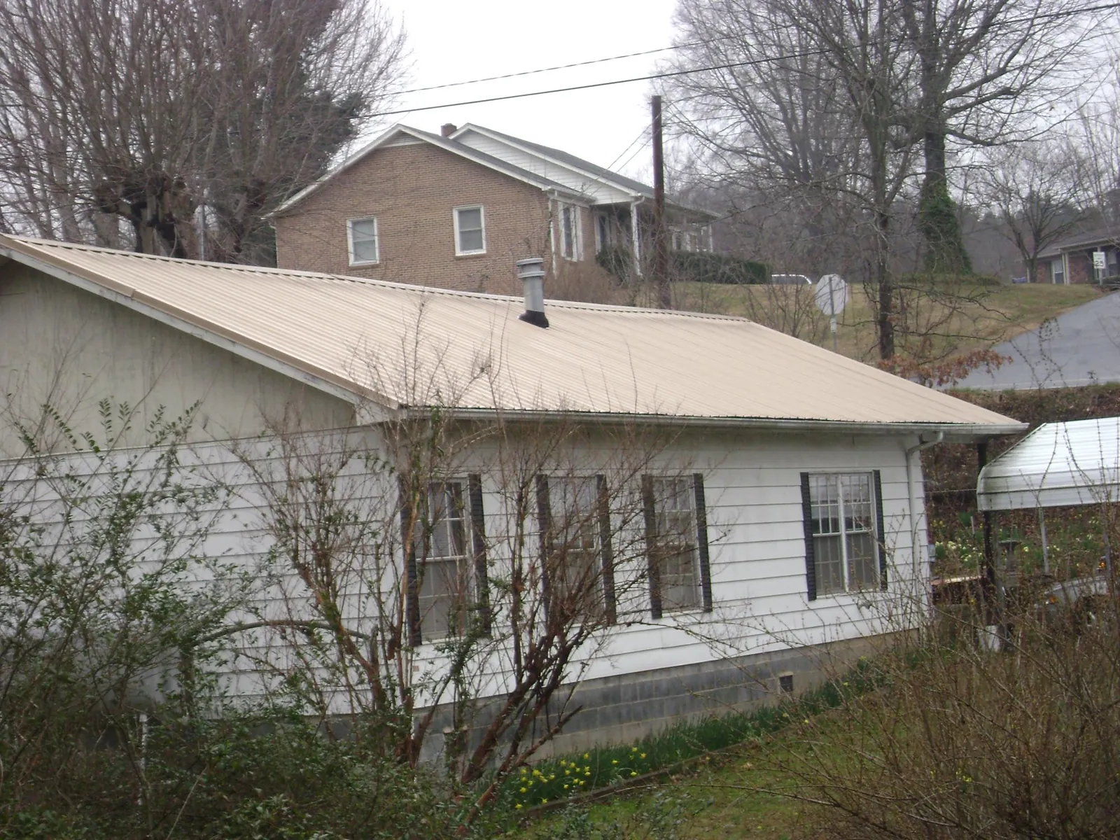 Tan metal roof on a white sided house set into a hillside — Commercial Roofing by Roofing Brothers in Malden